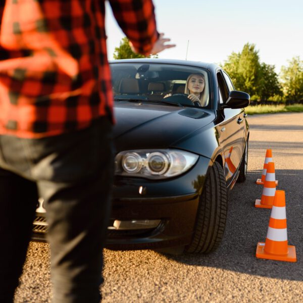 Female student passes between cones, lesson in driving school. Man teaching lady to drive vehicle. Driver's license education