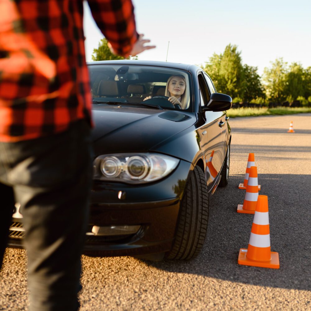 Female student passes between cones, lesson in driving school. Man teaching lady to drive vehicle. Driver's license education