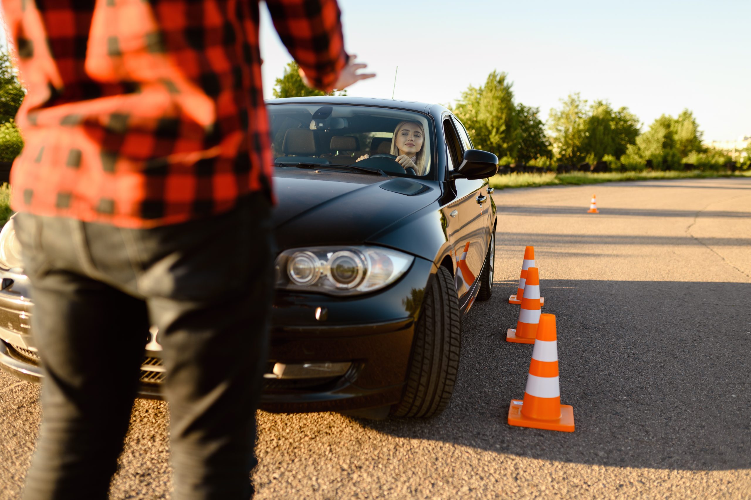 Female student passes between cones, lesson in driving school. Man teaching lady to drive vehicle. Driver's license education